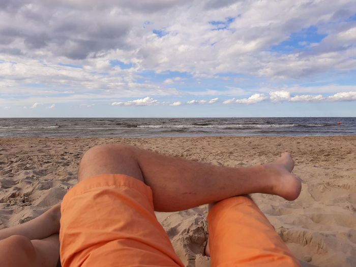 Low section of person relaxing on beach against sky