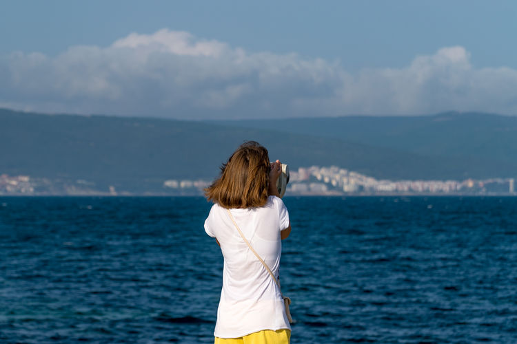 Rear view of woman standing by sea against sky