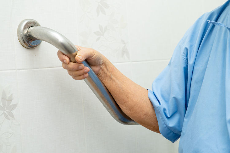 Midsection of senior woman holding railing by wall at bathroom