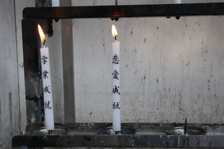 Close-up of lit candles with text burning in japanese temple