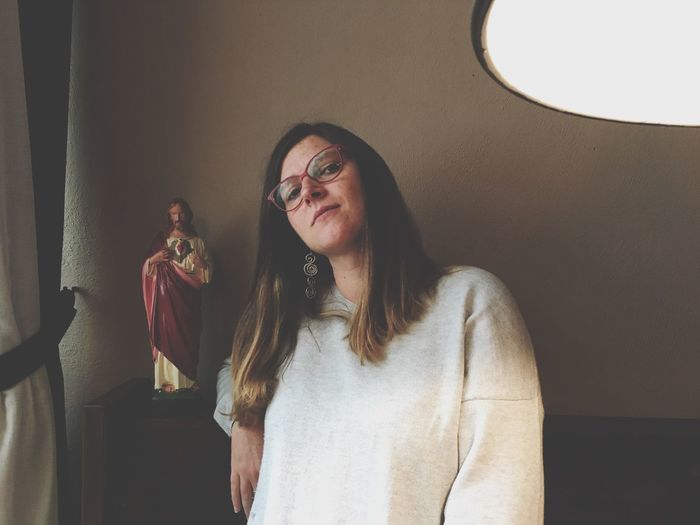 Portrait of woman standing by jesus christ figurine on table against wall