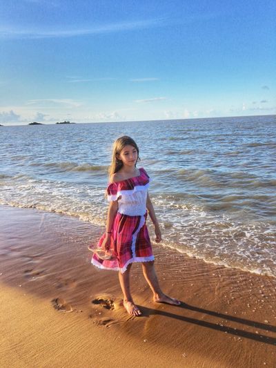 Full length of girl standing at beach against blue sky