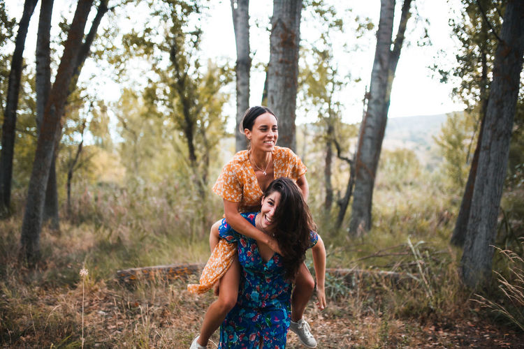 Woman piggybacking girlfriend in forest