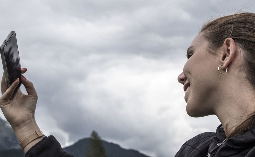 Smiling girl takes a selfie under a threatening gray sky in the mountain.