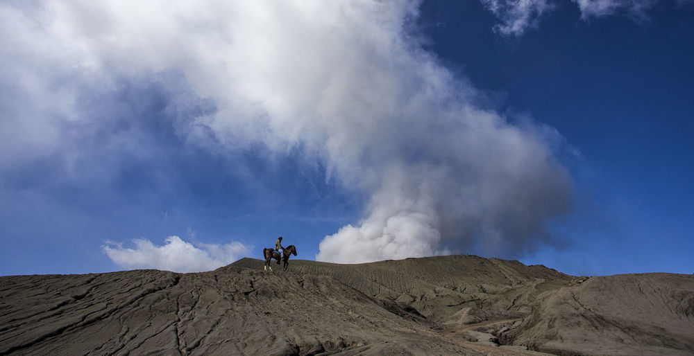 Mid distance view of person riding horse at mt bromo against blue sky