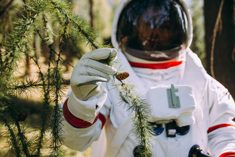 Astronaut holding plant in forest