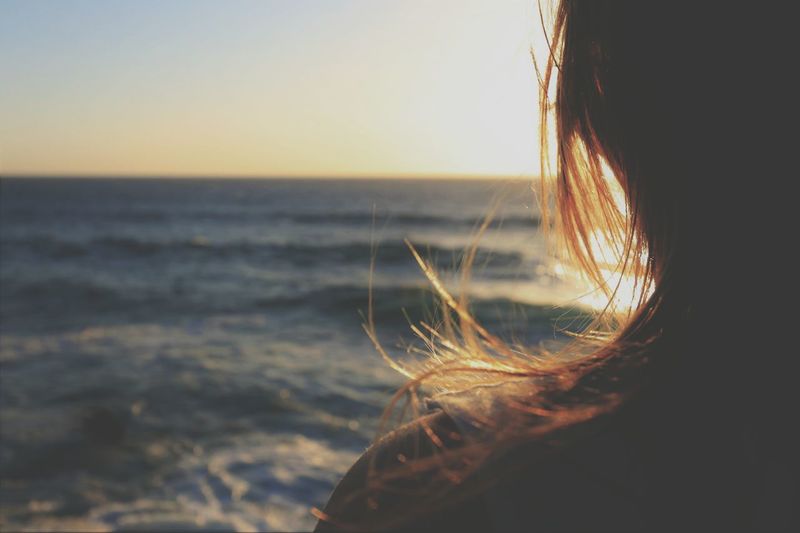 Cropped image of woman by sea during sunset