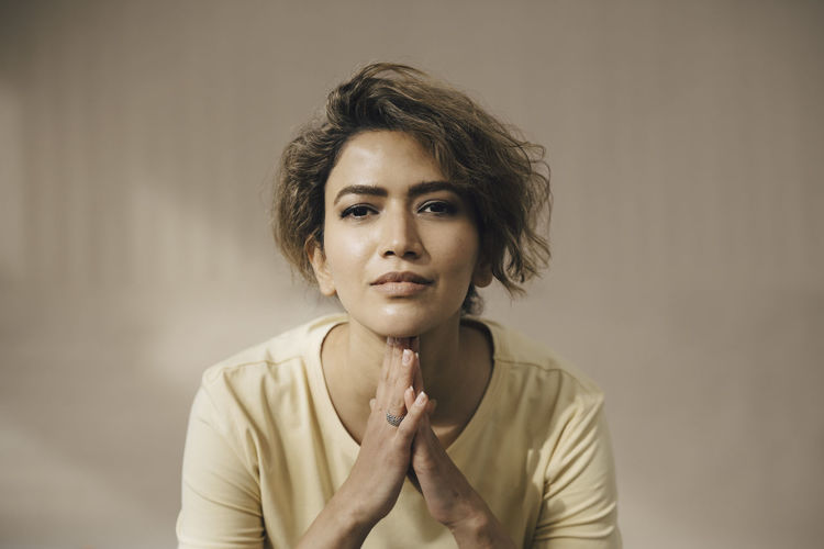 Woman with hands clasped against beige wall
