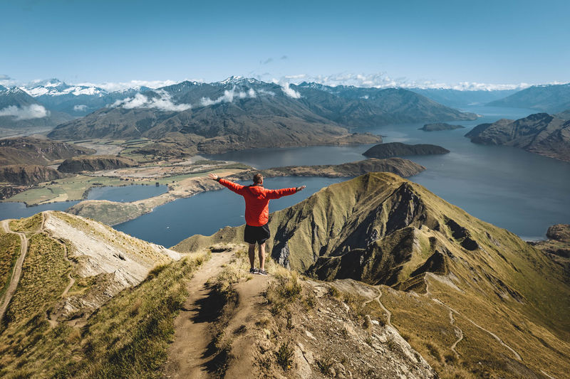 Rear view of man with arms outstretched standing against lake on mountain
