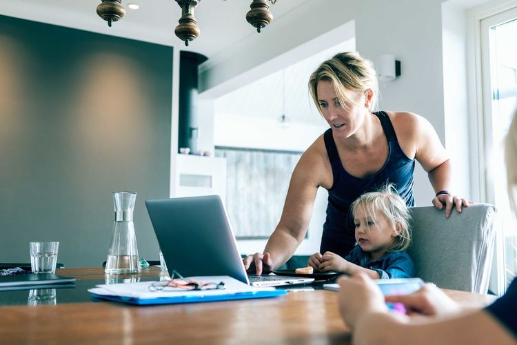 Mother using laptop while daughter sitting in living room at home