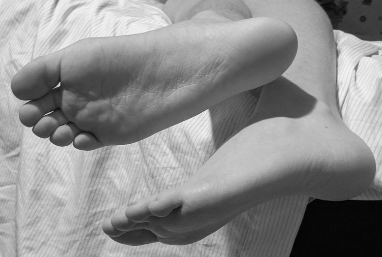 Black and white close-up of child's feet dangling from a bed at home