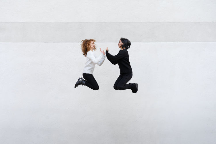 Side view of lesbian couple clapping hands while jumping against wall