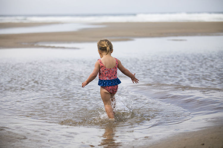 Rear view of young girl running through tidal pool at the beach.