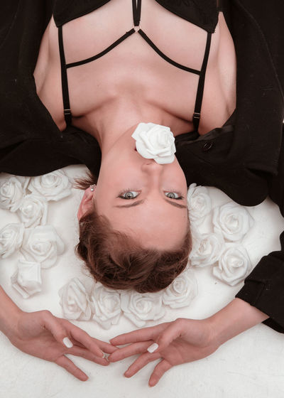 High angle portrait of young woman with white rose in mouth lying on bed
