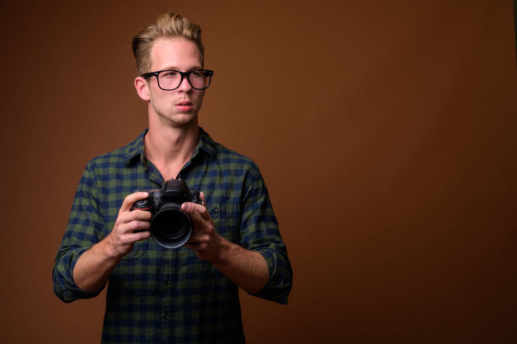 Young man holding camera looking away against colored background