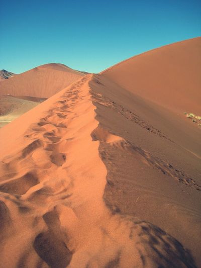 Sunlight falling on sand dune at desert against clear blue sky