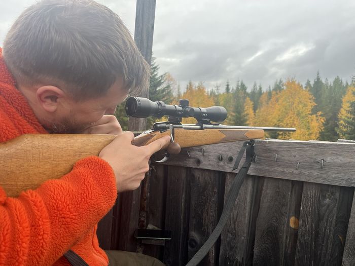 Side view of a man aiming with a rifle in a hunting tower during fall moose hunting season.