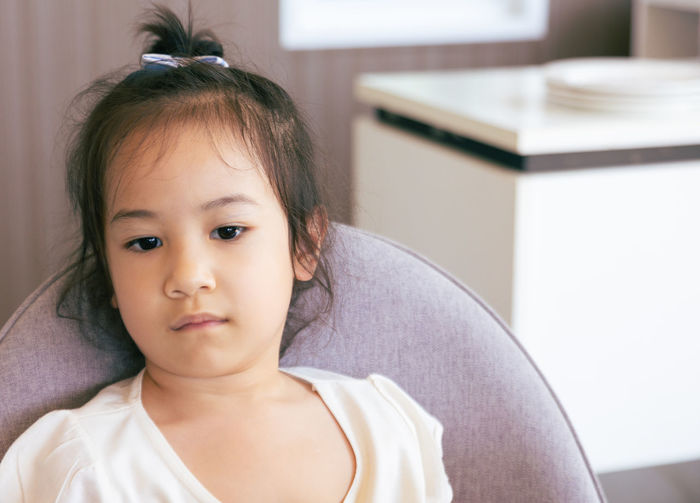 Girl portrait with copy space of adorable asian child sitting alone in the room with unhappy face