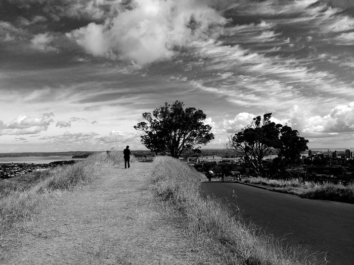 Man walking on road amidst field against sky