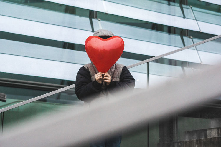 Person holding red heart shape on window