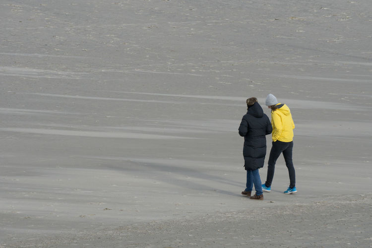 Rear view of women in warm clothes walking on beach