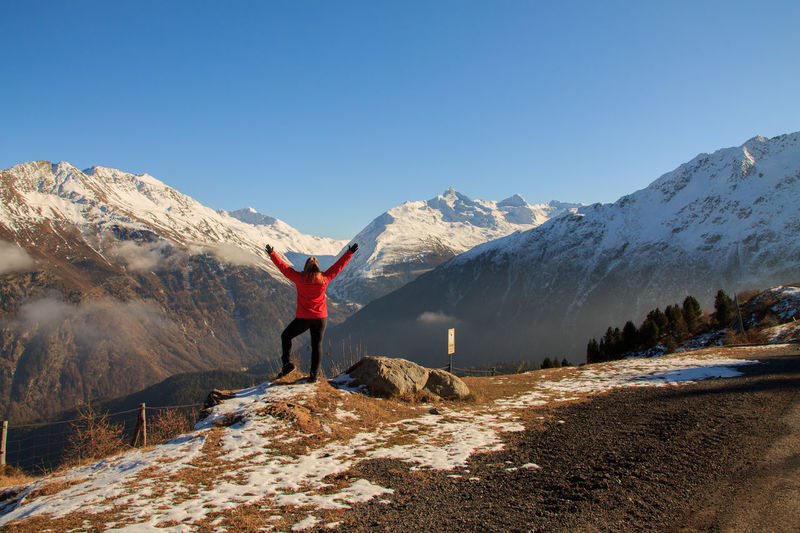 Rear view of woman with arms raised standing against snowcapped mountains