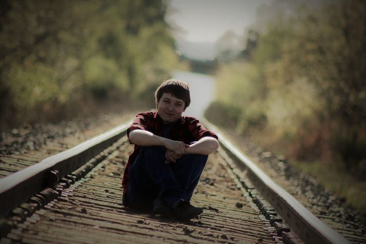Portrait of teenage boy sitting on railroad track