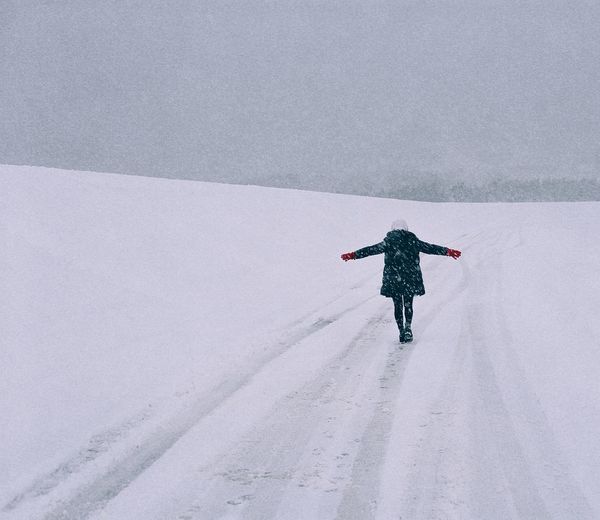 Full length rear view of woman walking on snowy field during snowfall