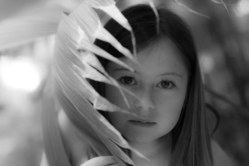 Close-up portrait of girl behind palm leaf