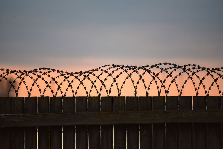 Silhouette of barbed wire fence against sky during sunset