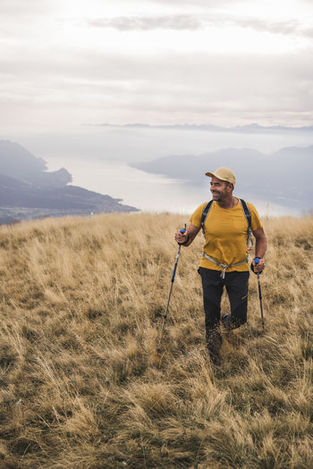 Smiling mature man wearing cap walking on grass with hiking poles