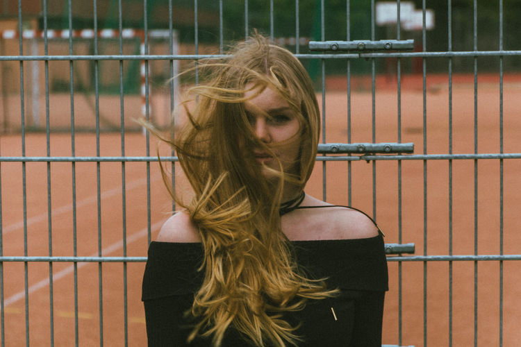 Portrait of young woman standing by metal fence