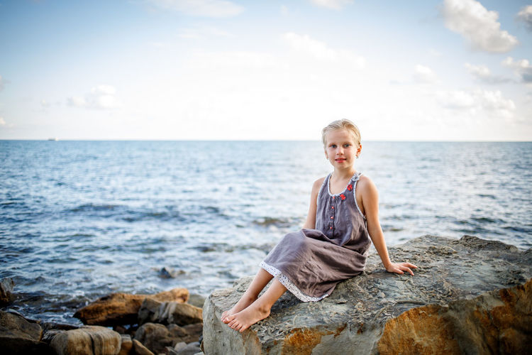 Portrait of smiling boy on rock at sea shore against sky