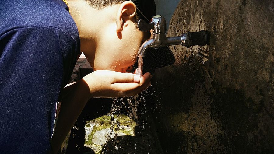 Side view of boy drinking water from faucet