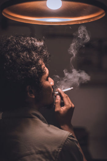 Man smoking cigarette in illuminated room
