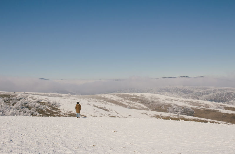 Rear view of woman standing on snow covered field by mountains against sky