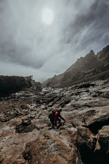 Person on rocks by mountains against sky