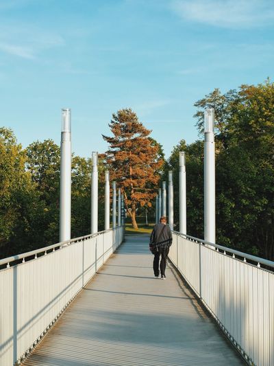Rear view of man walking on footbridge leading towards park