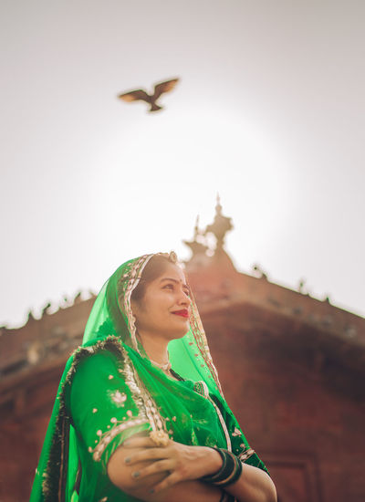 Portrait of smiling young indian woman standing against sky