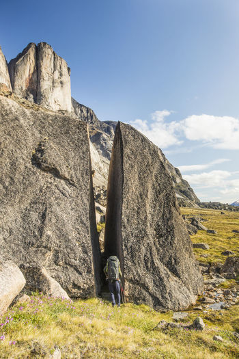 Backpacker squeezes through gap in cracked erratic boulder