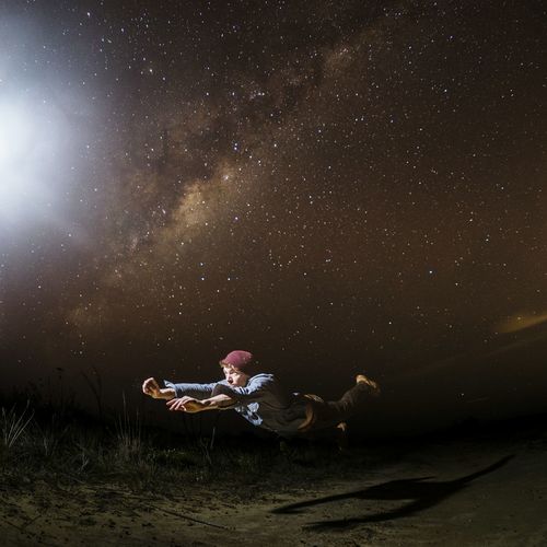 Young man levitating above field at night