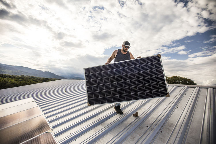 Electrician carries solar across roof during installation.