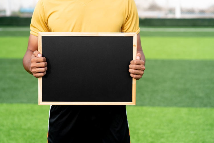 Midsection of man holding slate on soccer field 