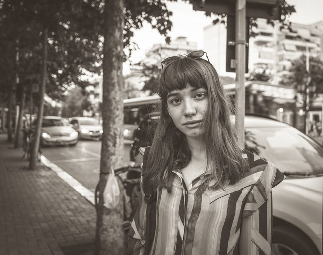 Portrait of woman standing on sidewalk in city