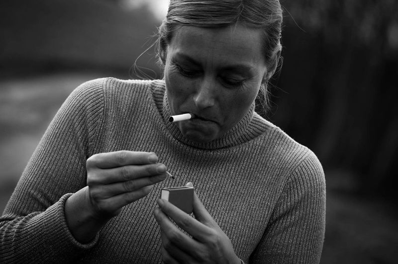 Close-up of young woman igniting cigarette with matchsticks