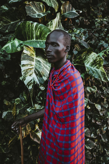 Maasai man in traditional clothes standing in front of green leaves