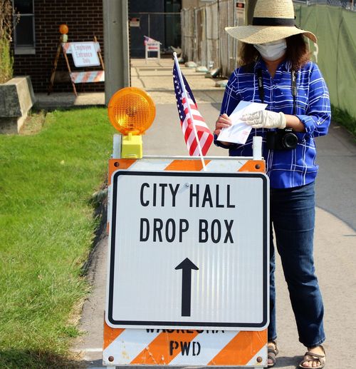 Senior woman wearing mask standing by drop box outdoors