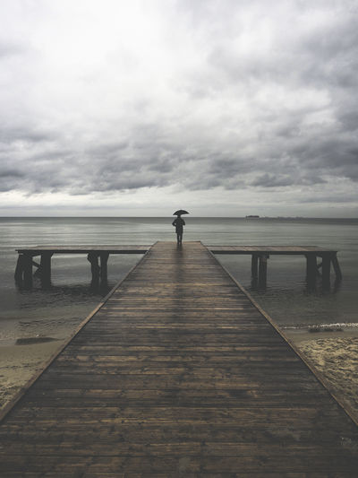 Man with umbrella standing at pier in dramatic mood