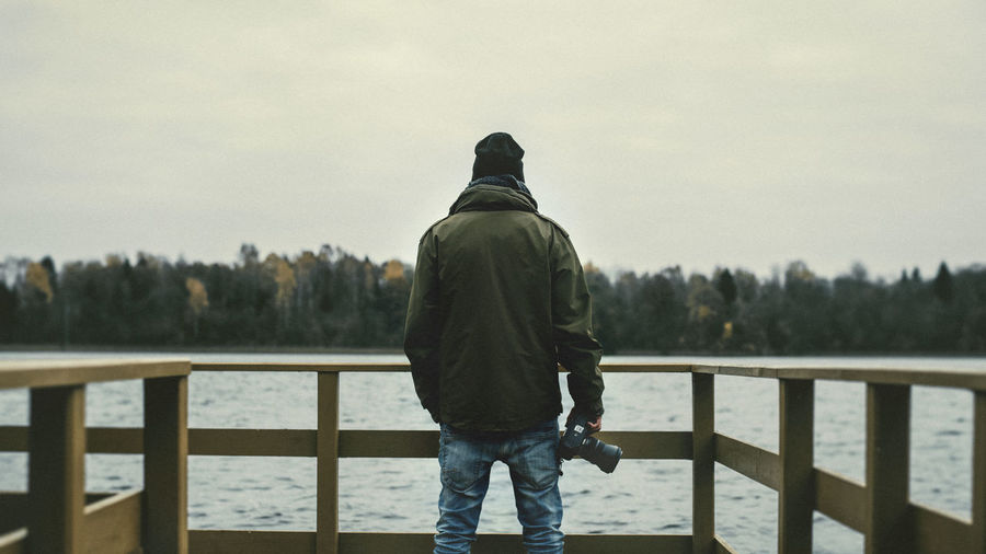 Rear view of man holding camera while standing on pier 