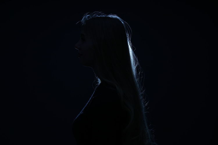 Side view portrait of young woman against black background